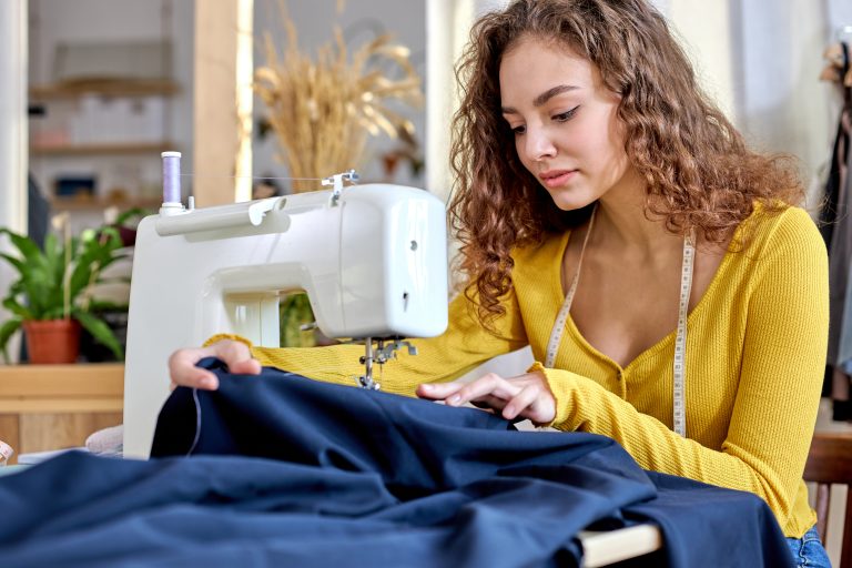 good-looking young tailor working on sewing machine, hand making clothes in home interior