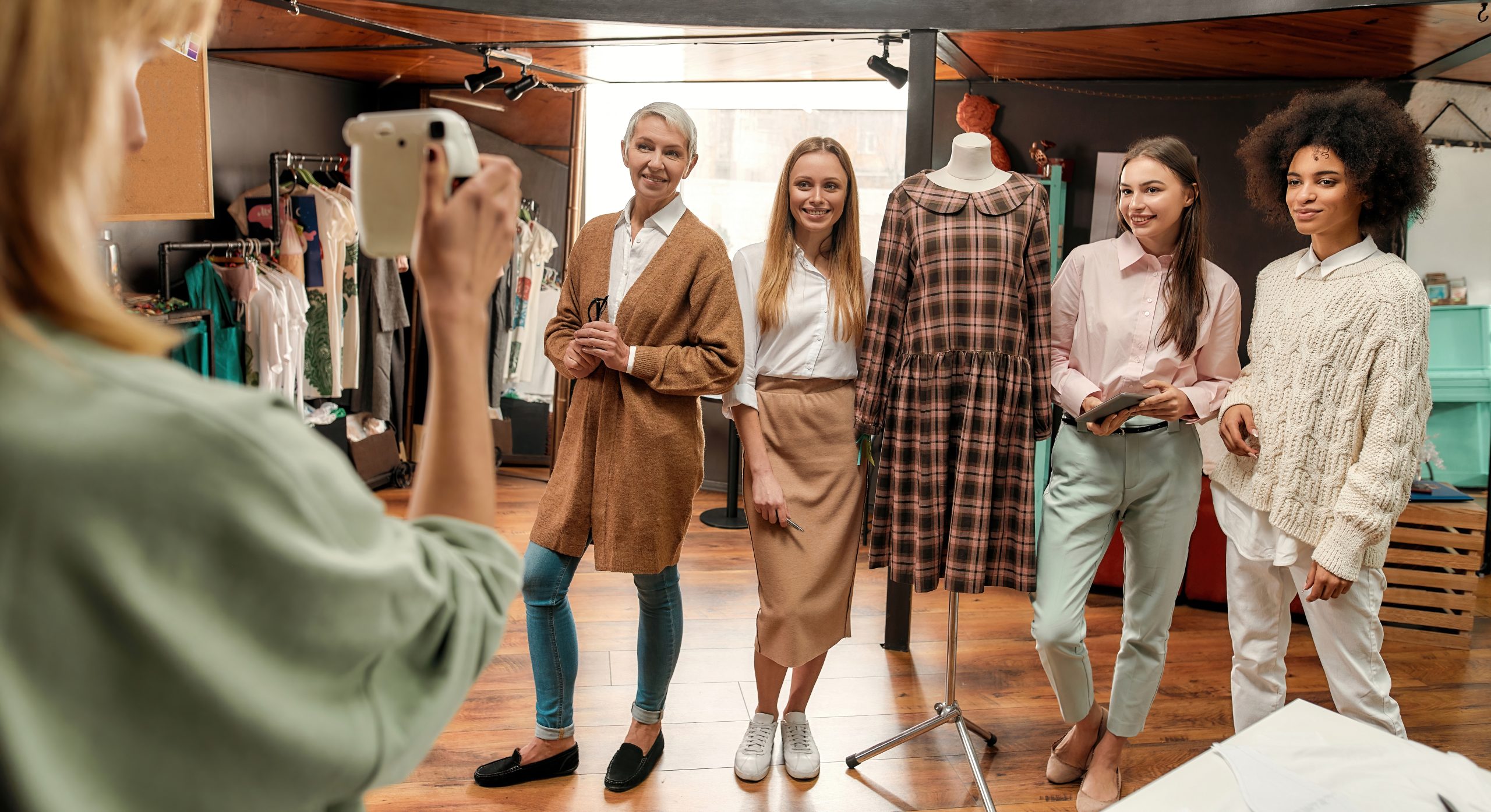 Group photo. Young woman making a photo of her fashionably dressed collaborateurs of different age and race in a big bright creative workshop